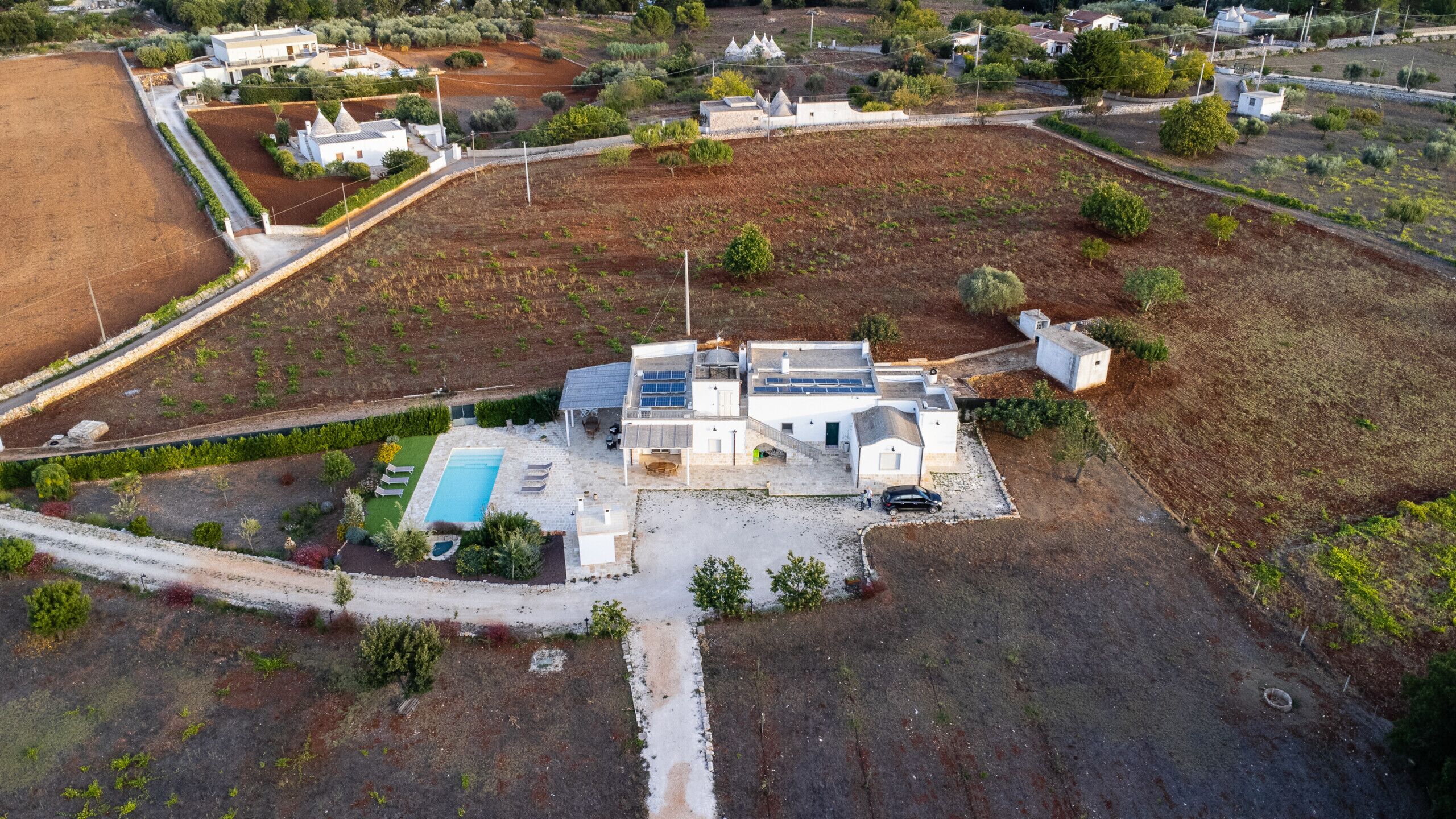 An aerial view of a modern house with a swimming pool, solar panels, and a well-maintained garden.