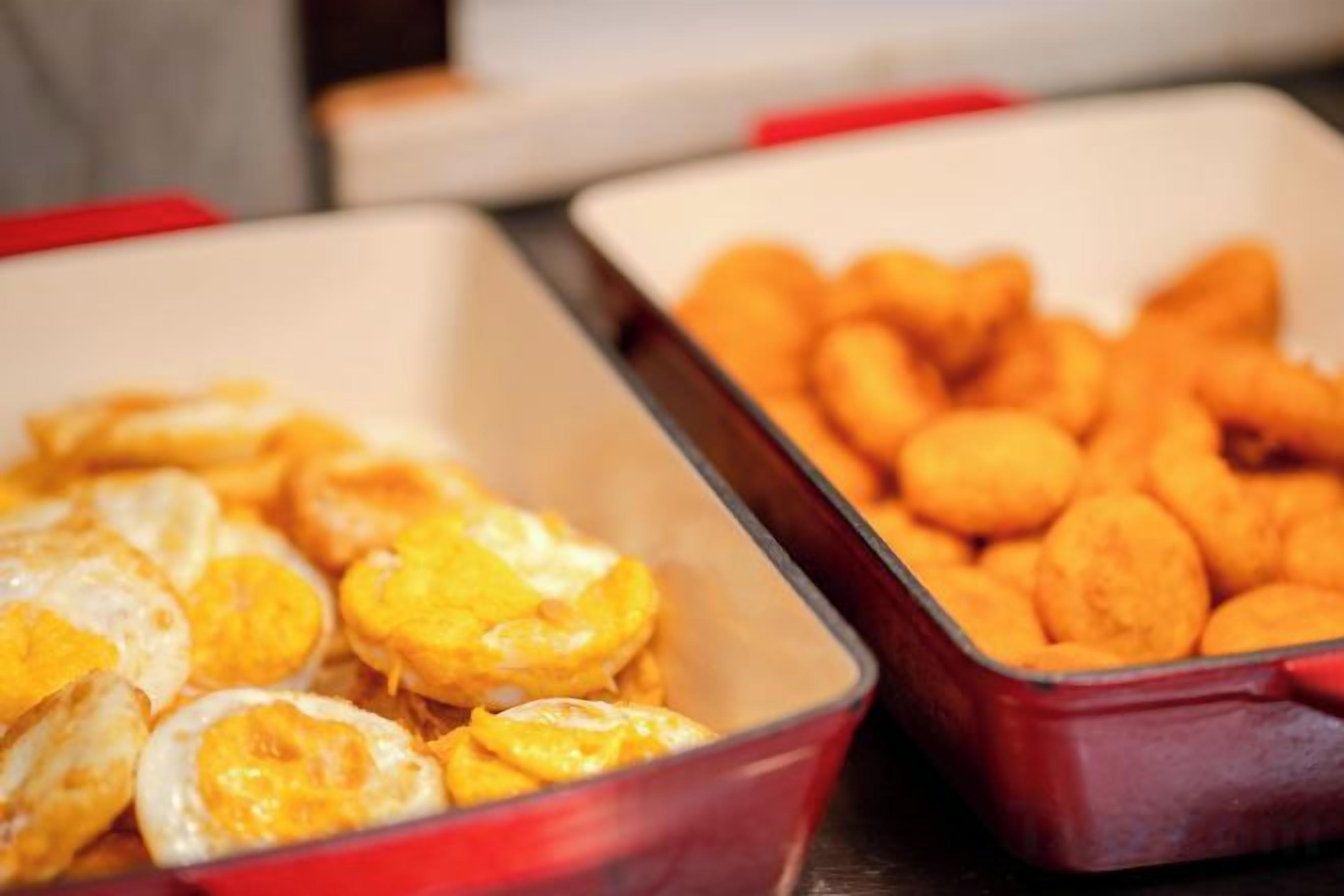Two containers with food items, one with sliced fruit and the other with fried snacks.