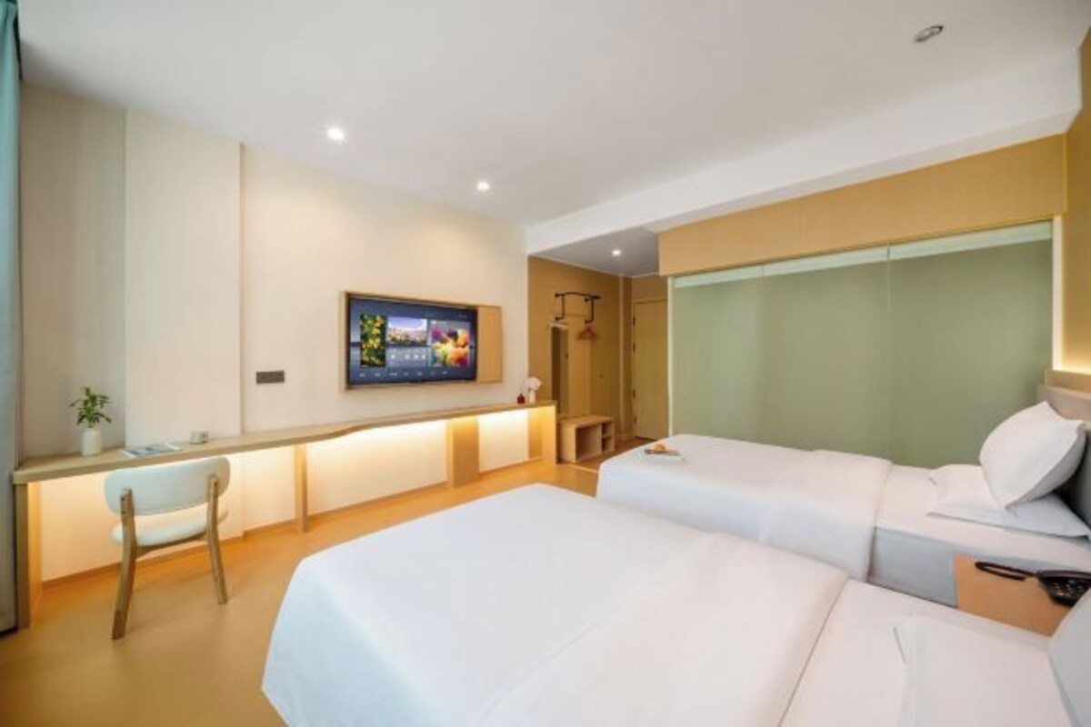 A hotel room with a bed, bedside table, chair, and a TV mounted on the wall.