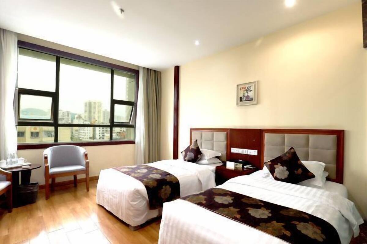 A hotel room with two beds, a desk, a chair, and a large window with a city view.