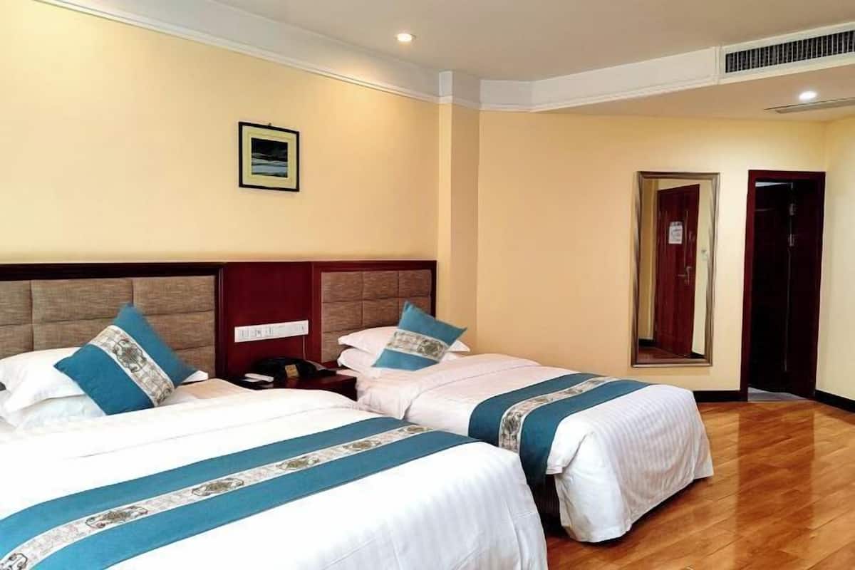 A hotel room with two beds, a wooden headboard, a nightstand, a framed picture on the wall, and a door with a mirror.