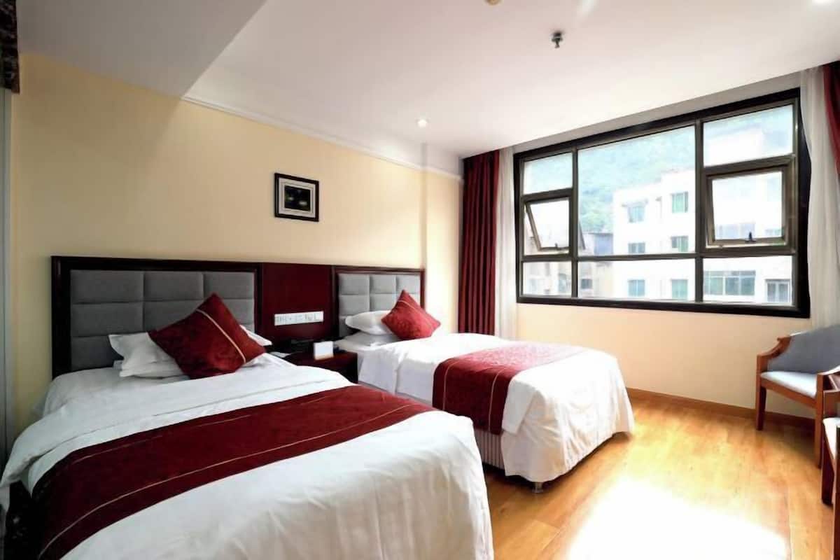 A hotel room with two beds, a window with curtains, a chair, and a framed picture on the wall.