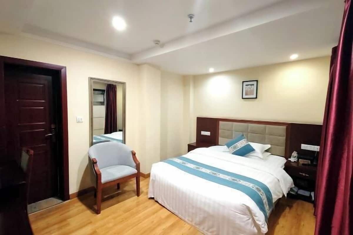 A hotel room with a bed, a chair, a nightstand, and a door.