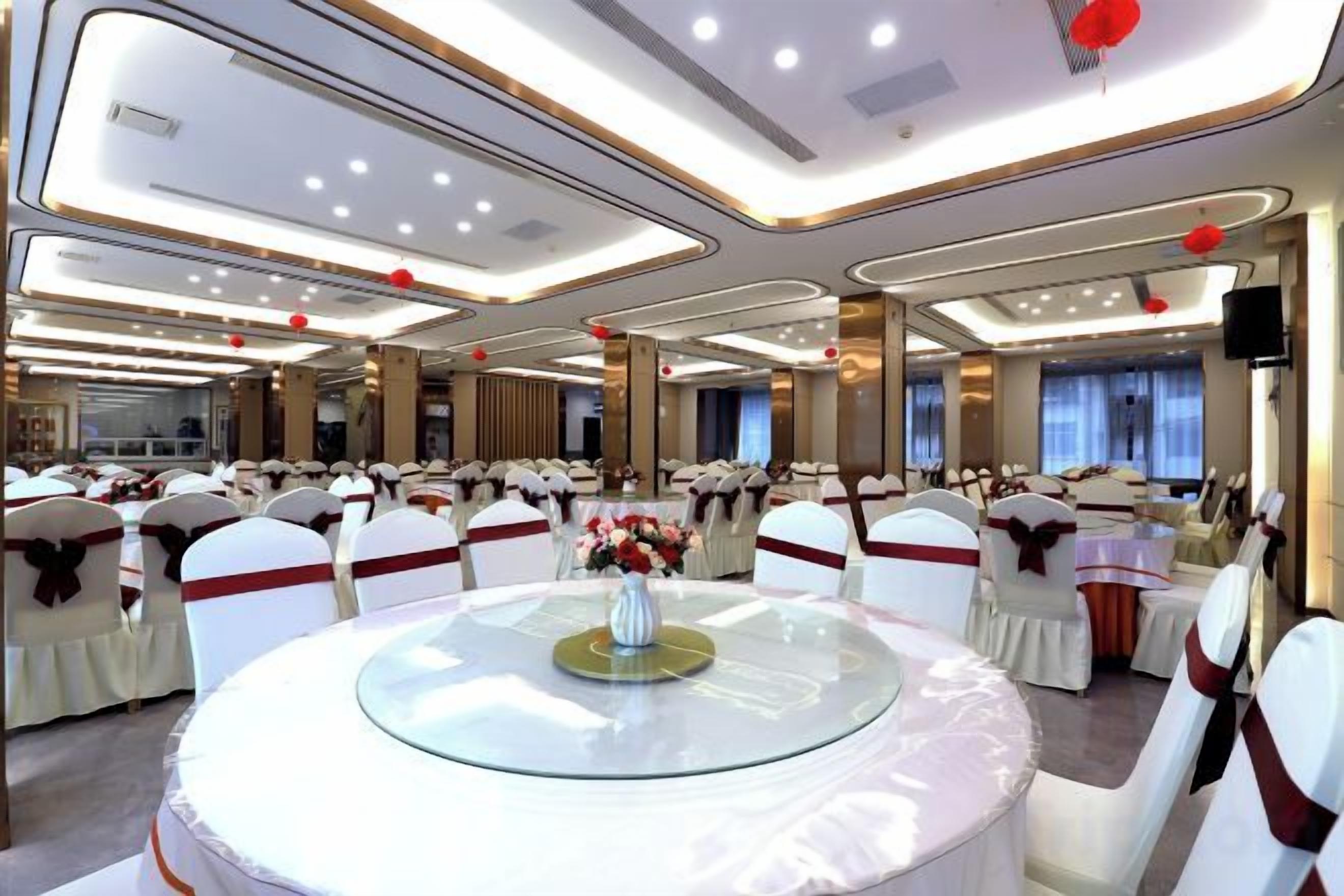 Une salle de banquet avec des tables rondes, des chaises blanches et des rubans rouges.