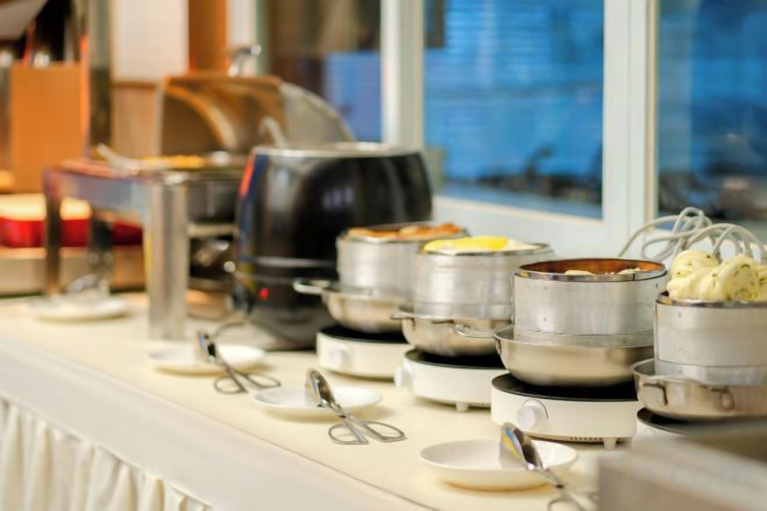 Un buffet est installé sur un comptoir, avec différents récipients contenant de la nourriture et des ustensiles à disposition.