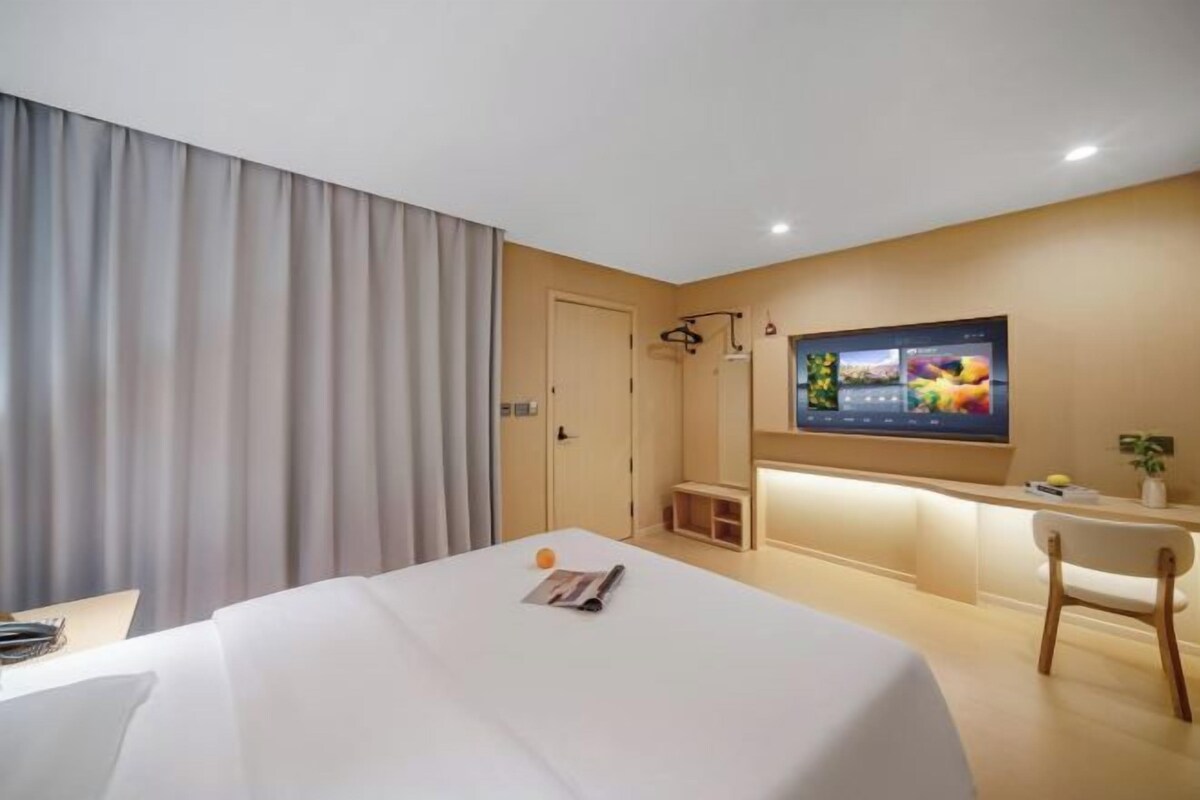 A hotel room with a bed, a desk, a television, and a window with curtains.