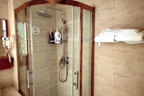 A glass-enclosed shower area with a handheld showerhead, a wall-mounted faucet, and a towel rack with folded towels. - Zhenghua Hotel (Zunyi)