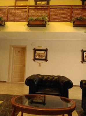 A lobby with a black leather sofa, a glass coffee table, wooden doors, and a decorative wall piece.