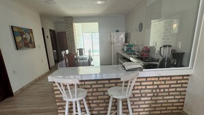 A modern kitchen with a central island, two white bar stools, and a brick accent wall.