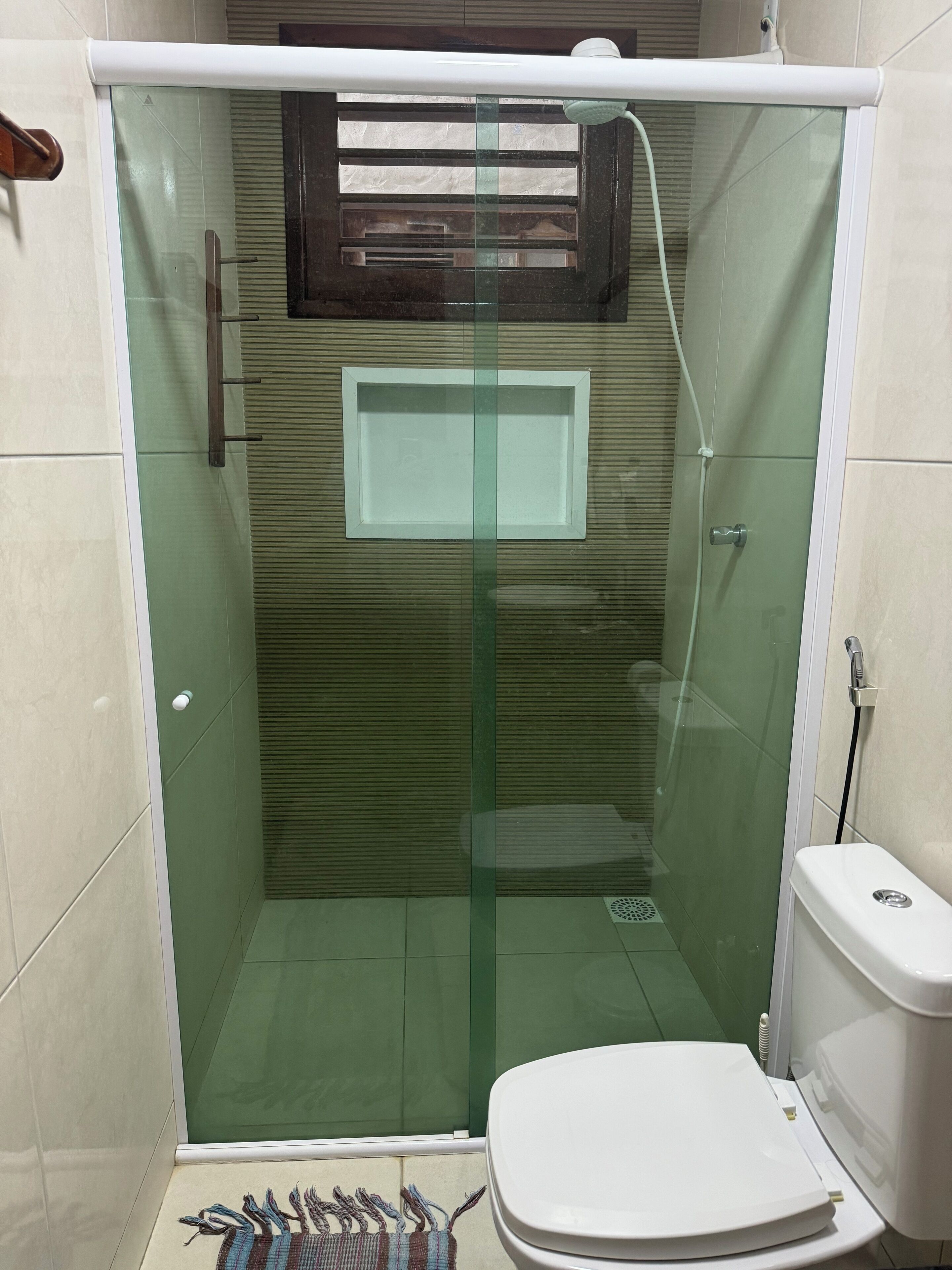 Une salle de bain moderne avec une douche à parois de verre, des toilettes et une petite fenêtre.