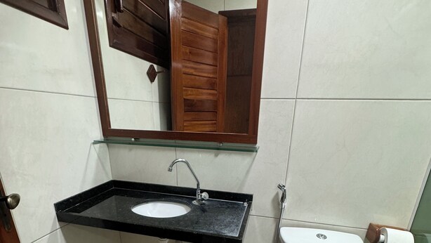 A bathroom with a sink, mirror, toilet, and a small trash bin.