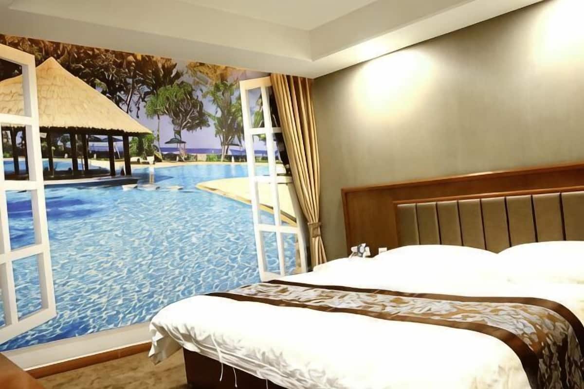 Ein Hotelzimmer mit Bett, Blick auf einen Swimmingpool und einem Reetdachgebäude.