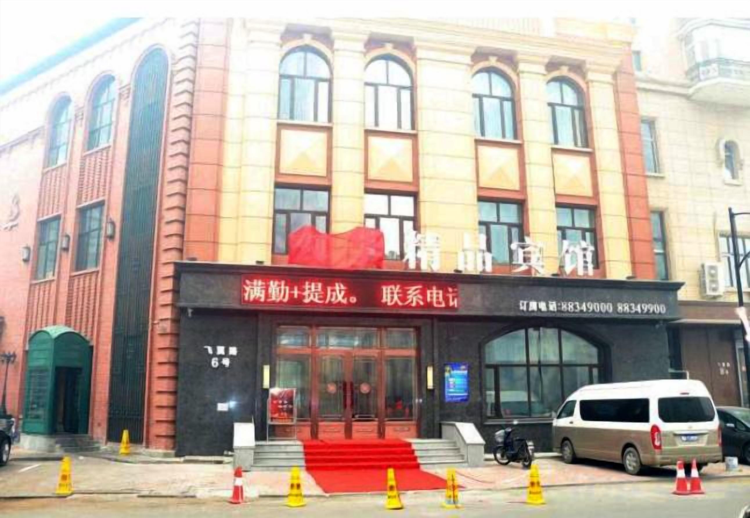 Un edificio con toldo rojo, un letrero con datos de contacto y una furgoneta estacionada al frente.