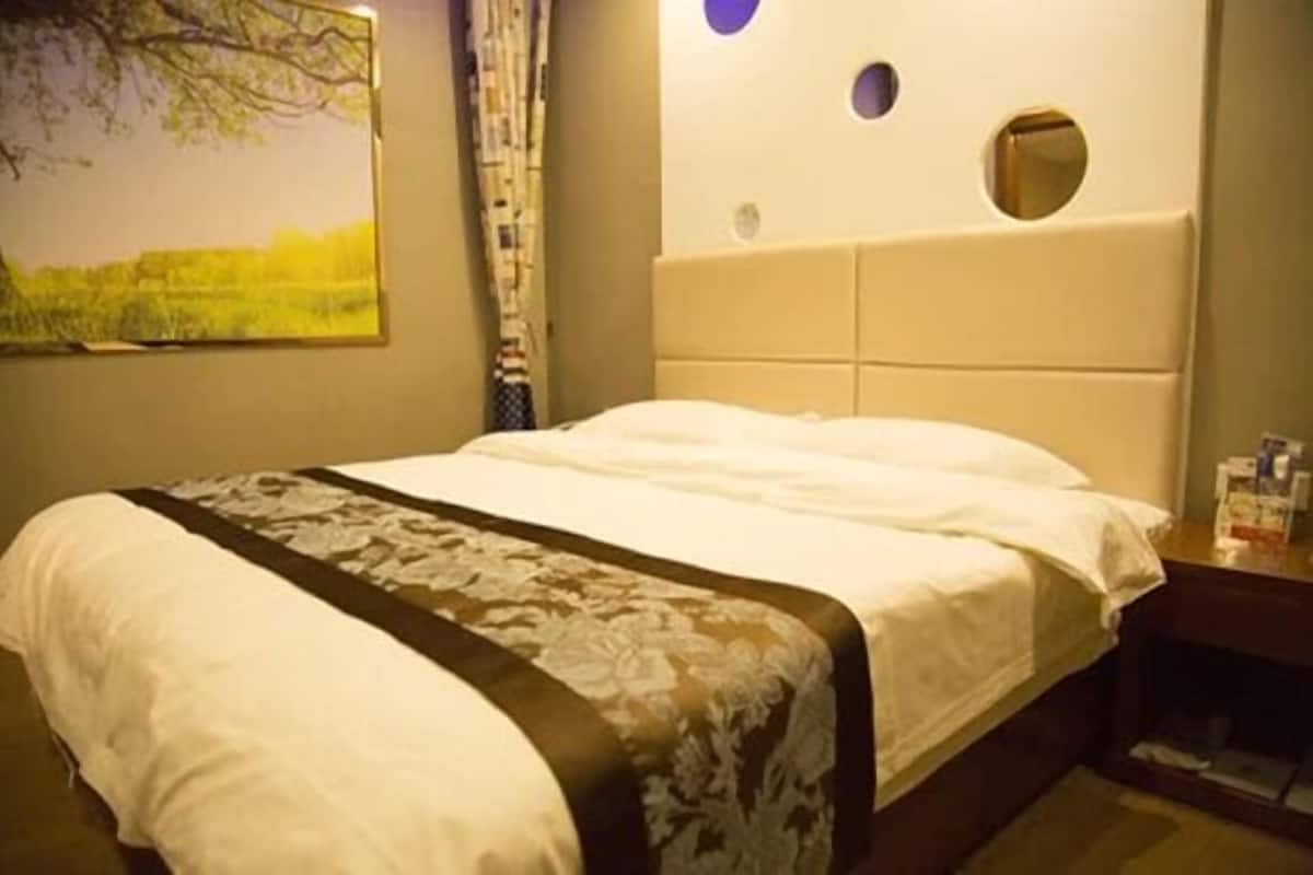 Ein ordentlich bezogenes Bett mit einem blumigen Überwurf, einem Kopfteil mit runden Ausschnitten und einem Landschaftsbild an der Wand.