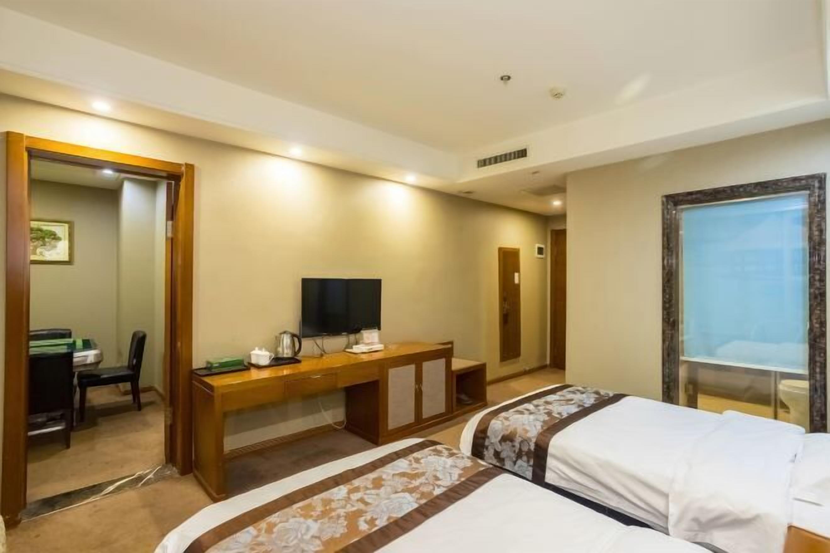 A hotel room with a bed, a desk with a television, a mirror, and a window.