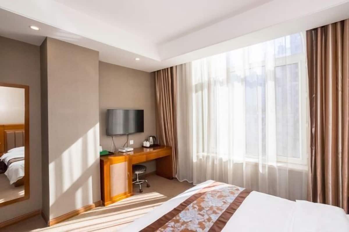 Ein Hotelzimmer mit Bett, Schreibtisch, Fernseher und einem großen Fenster mit Vorhängen.