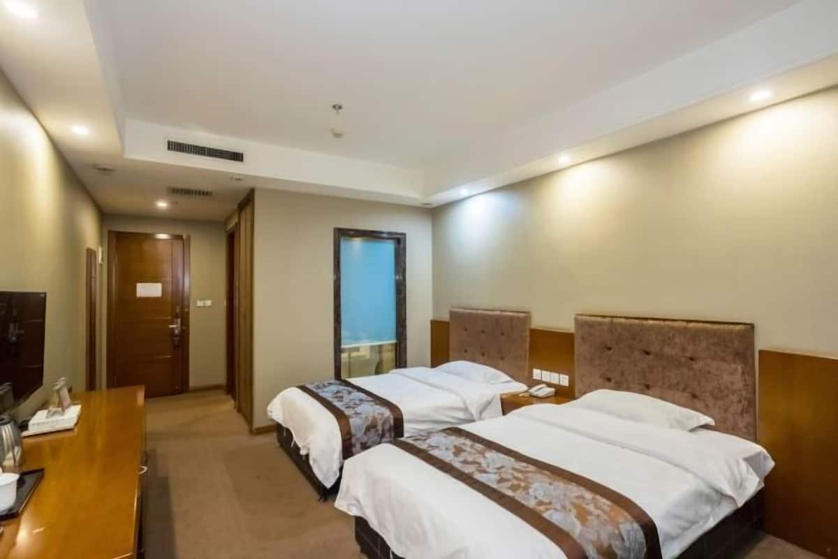 Ein Hotelzimmer mit zwei Betten, einem Holztisch, einem Fernseher und einer Tür zu einem anderen Raum.