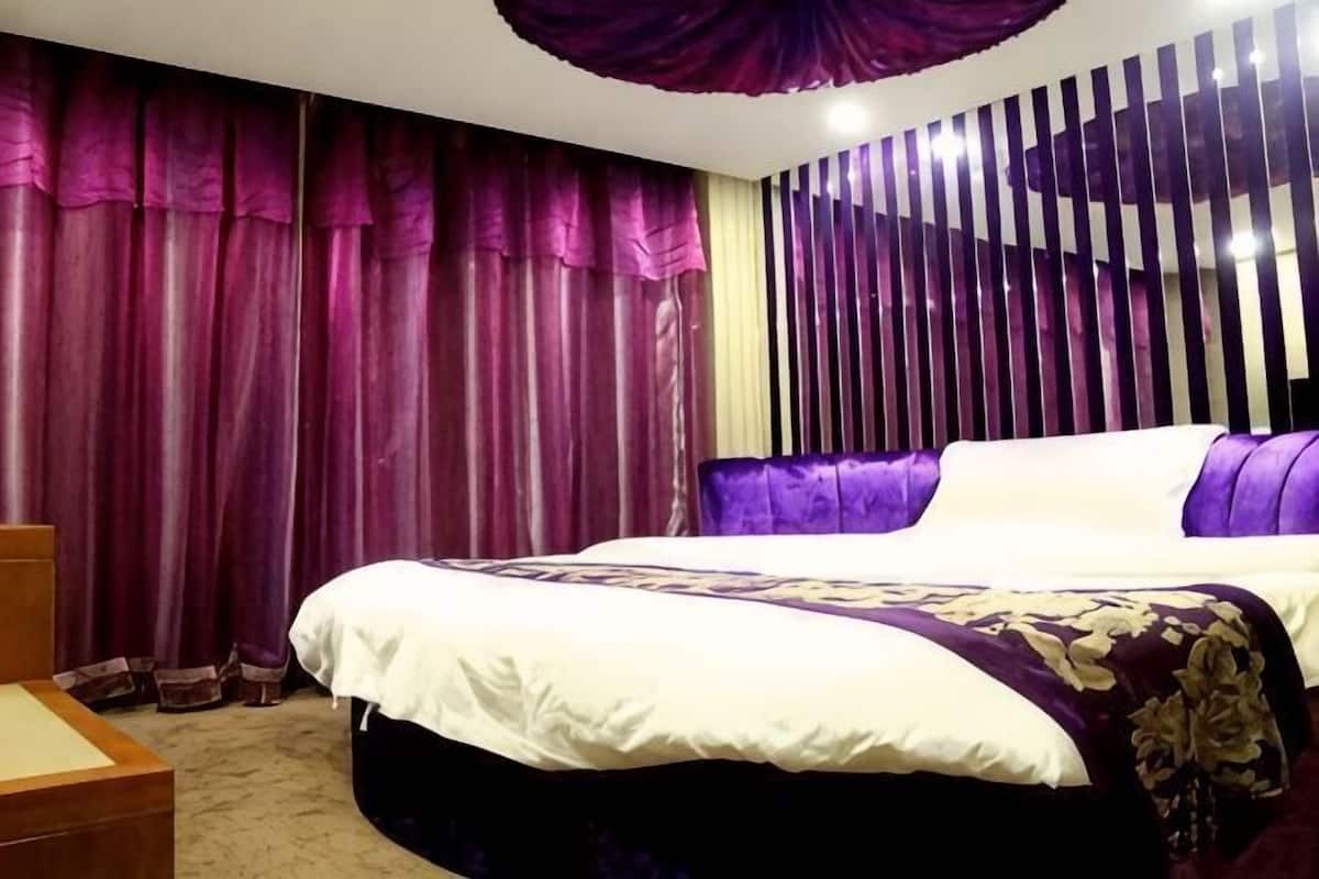 Ein Hotelzimmer mit einem großen Bett, einem Holfnachtisch und einem fensterhohen Vorhang.