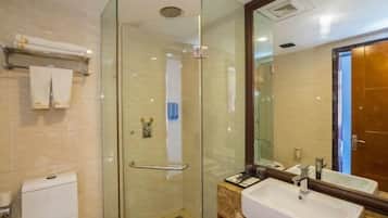 A modern bathroom with a glass shower enclosure, a toilet, a sink with a marble countertop, and a large mirror.