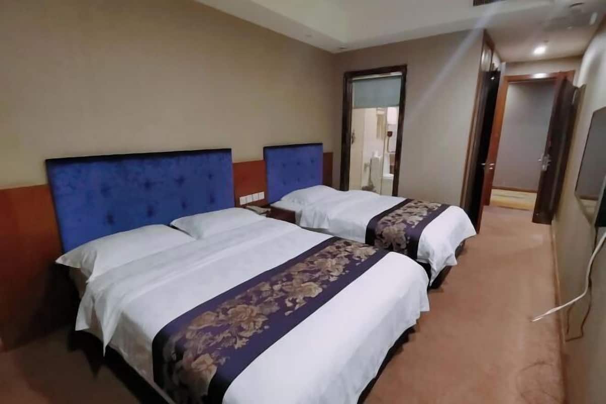 Ein Hotelzimmer mit zwei Betten, jeweils mit blauem Kopfteil und weißer Bettwäsche.