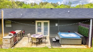 Un patio trasero con porche techado, jacuzzi, parrilla y mesa con sillas.