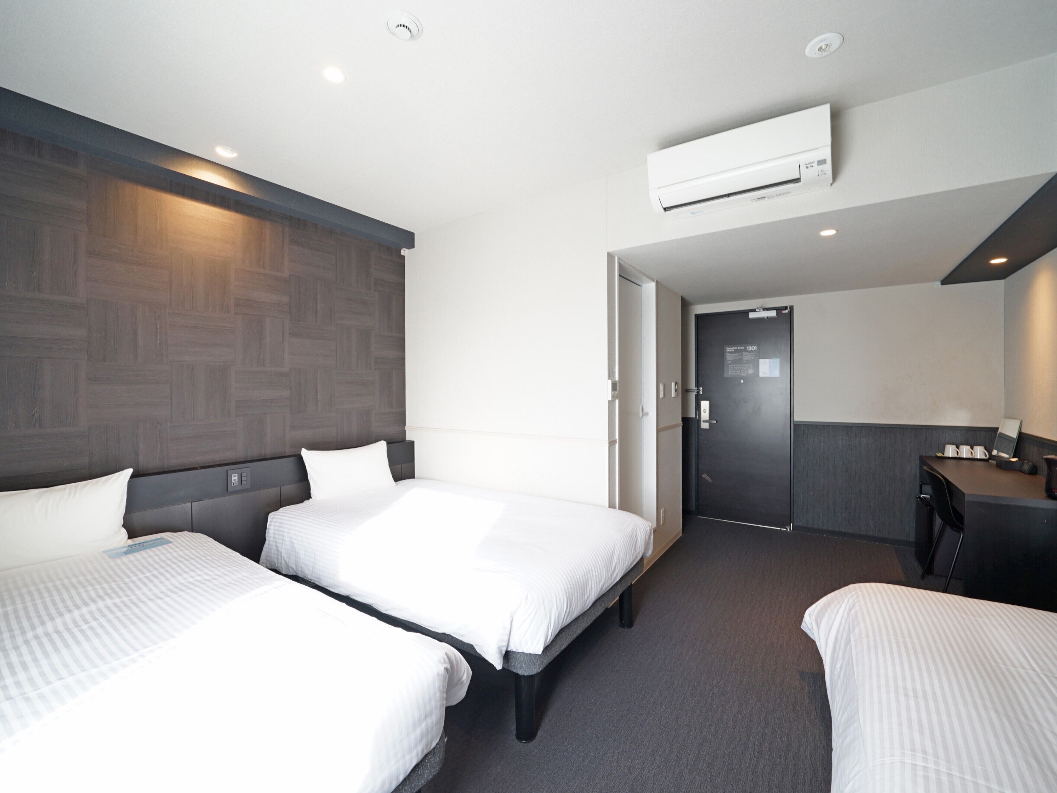 A hotel room with two beds, a desk, and an air conditioning unit.