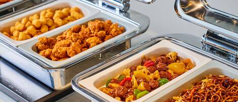 Ein Buffet mit verschiedenen Speisen, darunter gebratenes Hähnchen, Pasta mit Gemüse und Nudeln.