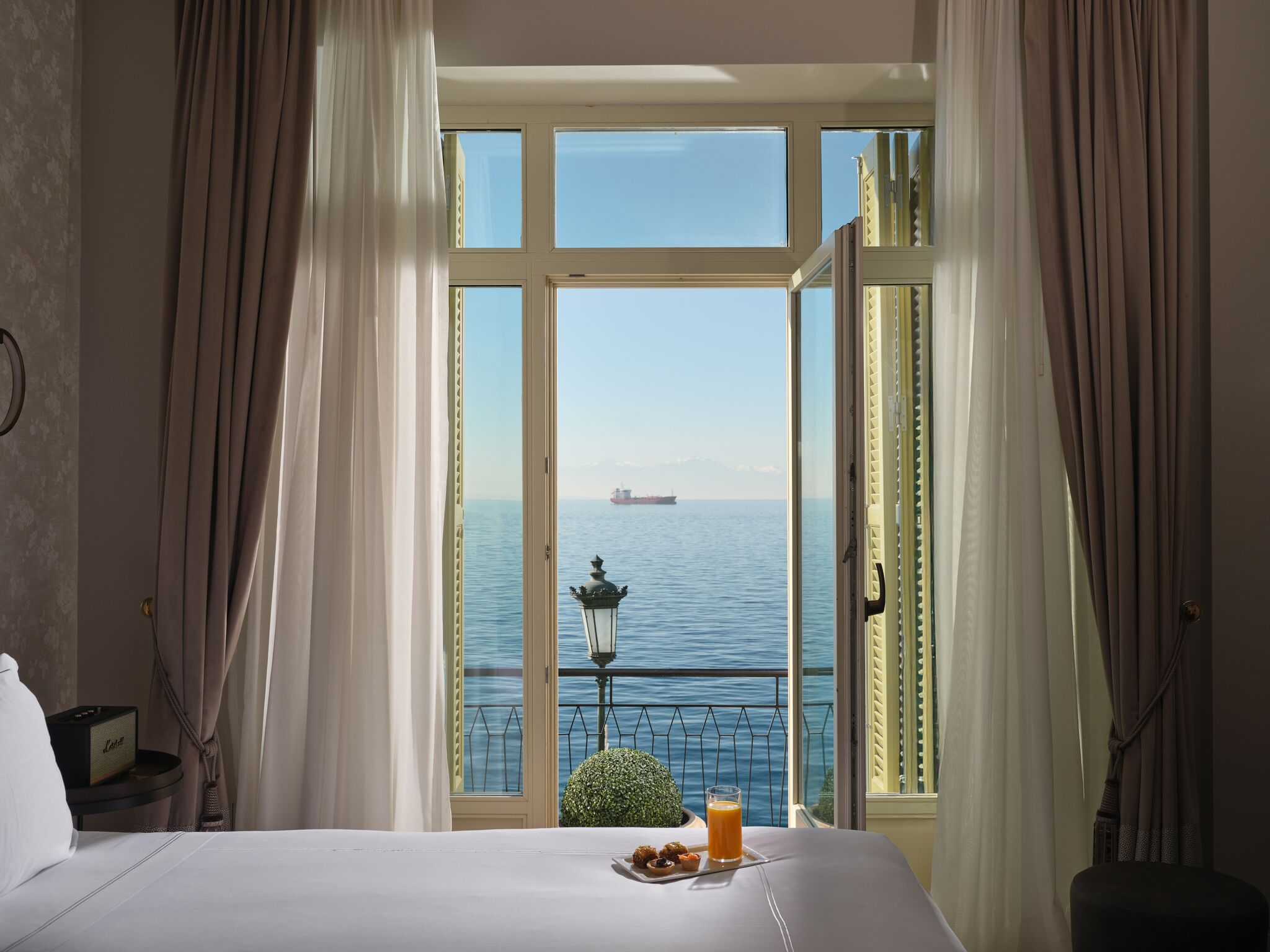 Quarto de hotel com uma janela grande, uma cama, uma mesa pequena com café da manhã e vista para o mar.