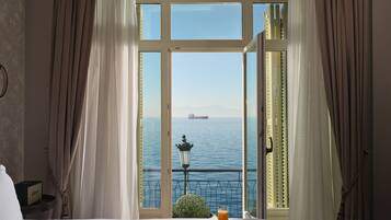 Quarto de hotel com uma janela grande, uma cama, uma mesa pequena com café da manhã e vista para o mar.