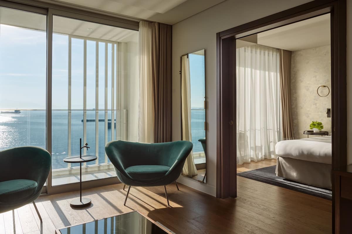 A modern hotel room with a large balcony, a bed, a small table, and a chair.