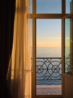 An open door with a view of the sea and a balcony with a metal railing.