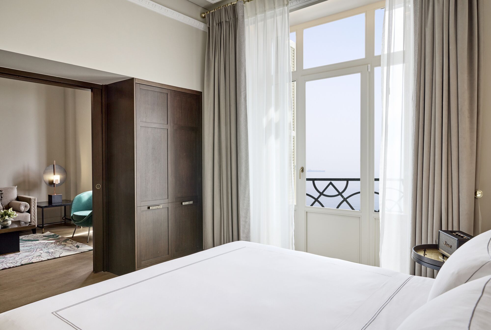 Habitación de hotel con una cama grande, un armario, un escritorio con lámpara, una silla y vistas al balcón.