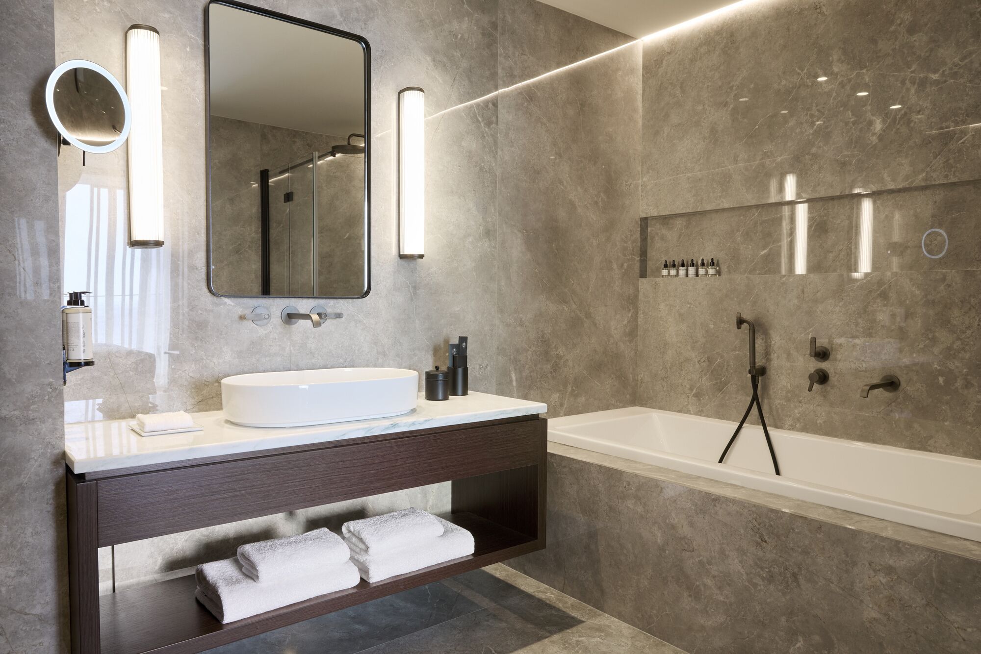 Une salle de bain moderne avec un grand miroir, un lavabo blanc, un meuble-lavabo foncé et une baignoire.