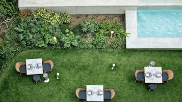 A poolside area with a hot tub, two dining tables with chairs, and lush greenery.