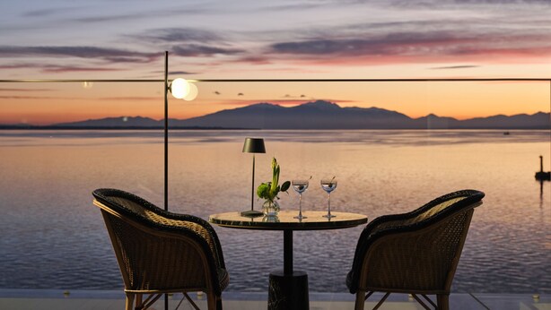 A table with two chairs facing a body of water, a lamp, and two glasses. - ON Residence (Thessaloniki)