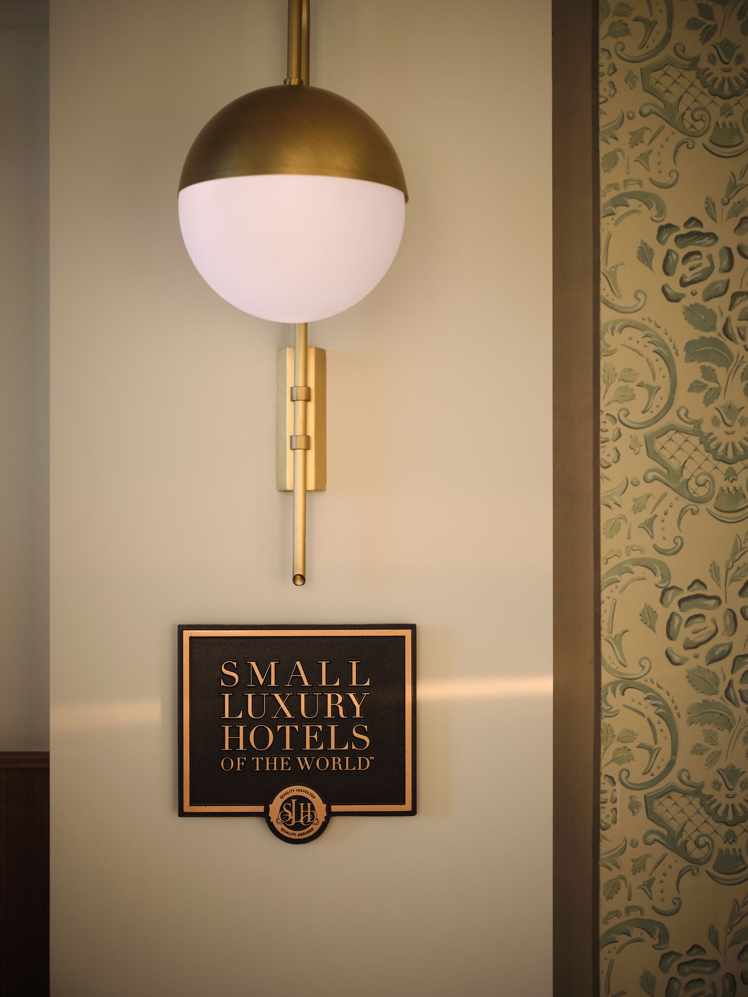 A wall-mounted light fixture with a spherical shade and a sign below stating 'SMALL LUXURY HOTELS OF THE WORLD'.