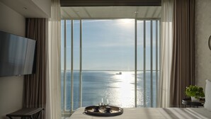 A bedroom with a large window, a bed, a bedside table, a TV, and a tray with cups and a glass. - ON Residence (Thessaloniki)
