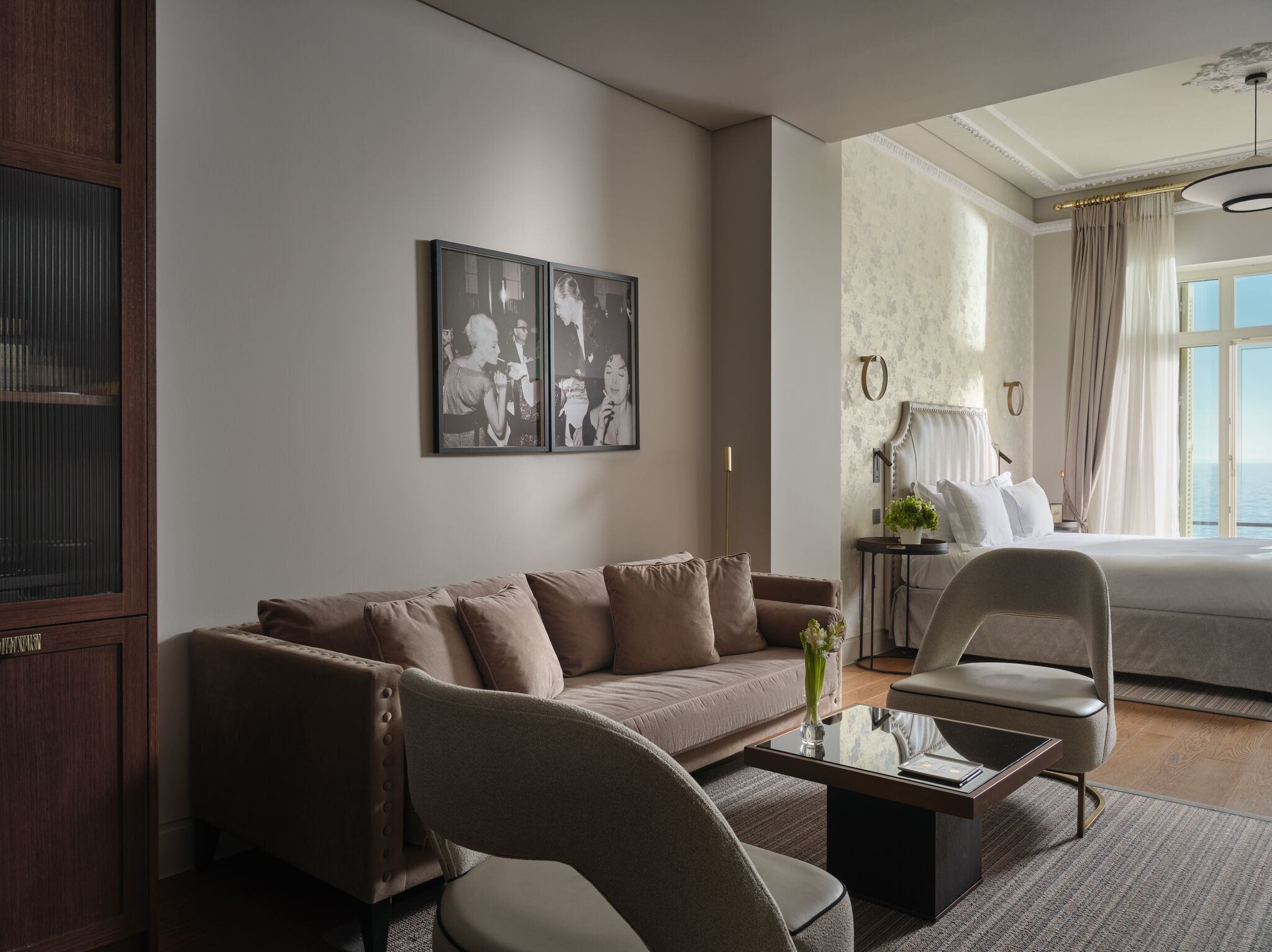 Une chambre d’hôtel avec un canapé, un fauteuil et un lit. Un tableau encadré est accroché au mur, et il y a une fenêtre avec des rideaux.