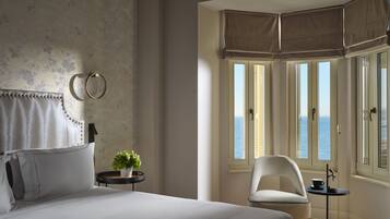 Ein Schlafzimmer mit einem Bett, einem Sessel, einem kleinen Tisch, einer Topfpflanze und Meerblick durch große Fenster.