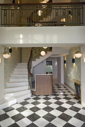 A grand staircase with a checkered floor, a wooden railing, and wall sconces.