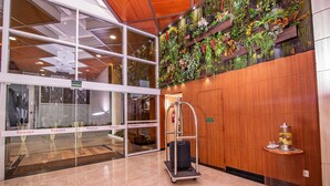 A hotel lobby with a glass entrance, a luggage cart, a water dispenser, and a wall with vertical gardens. - Ramada by Wyndham Manaus Torres Center (Manaus)