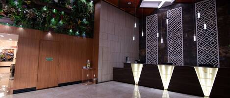 Un vestíbulo de hotel moderno con un mostrador de recepción de madera, un jardín vertical verde y un muro con diseño.