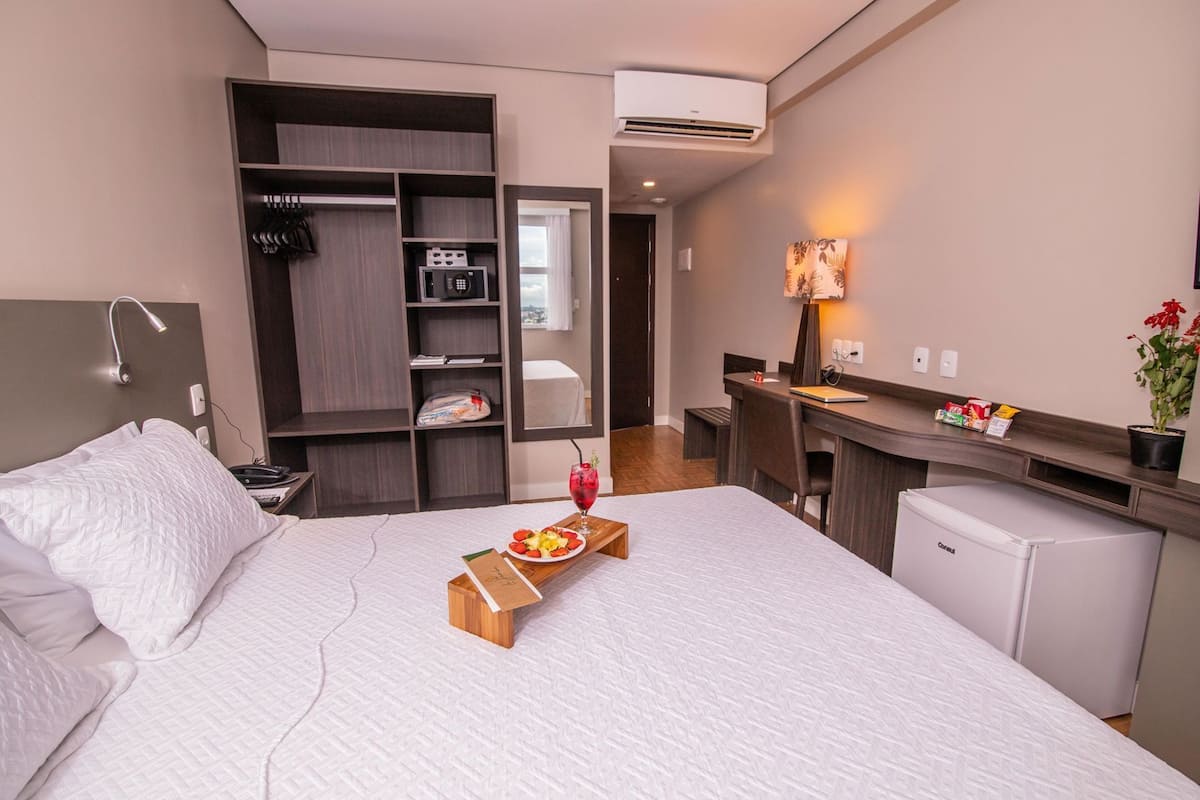 A hotel room with a bed, a desk, a mini-fridge, a wardrobe, and a bathroom.