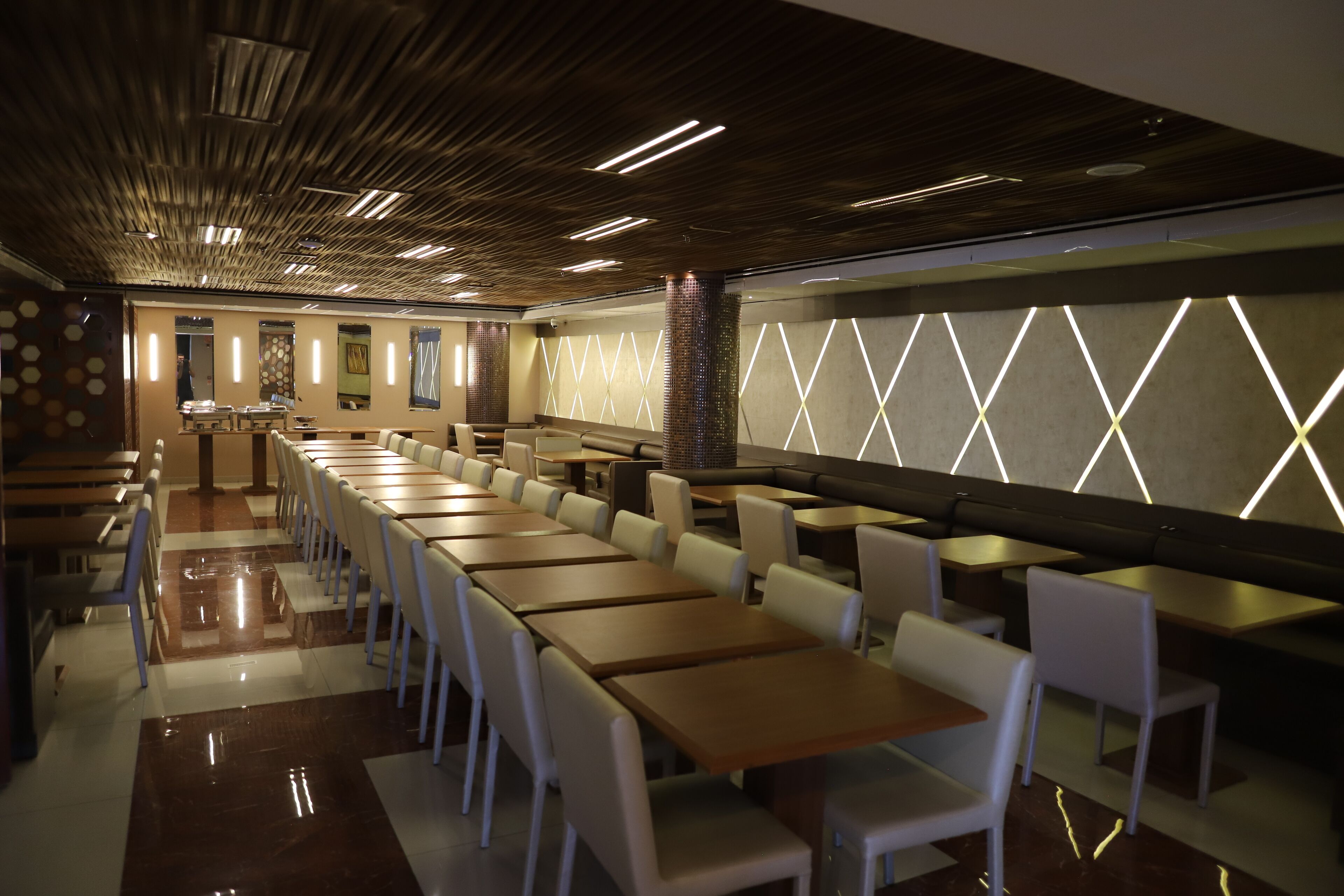 Un restaurante moderno con mesas largas y cabinas, un techo con diseño y una pared con iluminación geométrica.