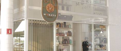 Een koffiebar met een grote glazen gevel, een bord met de tekst 'MOKAYA coffee' en een zitgedeelte met stoelen buiten.