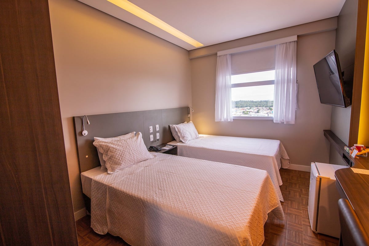 A hotel room with two beds, a TV, a window with curtains, and a wooden floor.