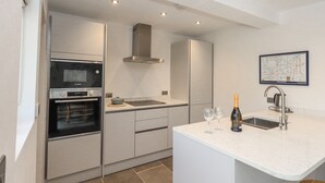 Una cocina moderna con horno empotrado, campana extractora de acero inoxidable, un fregadero y una botella de vino.