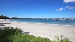 Une plage de sable blanc bordée d’une eau d’un bleu cristallin. Plusieurs voiliers sont amarrés dans l’eau.