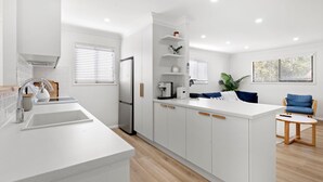 Une cuisine moderne avec des meubles blancs, un îlot central intégré et un coin salon agrémenté d’une chaise bleue.