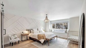 A bedroom with a bed, bedside table, chair, and crib.
